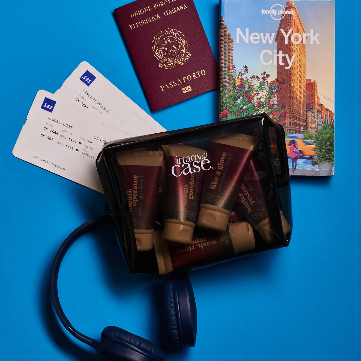 La beauty bag con i sette prodotti dentro, accanto a passaporto, carta d'imbarco e cuffie